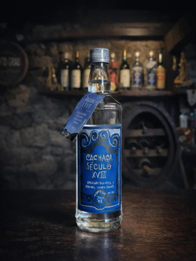 Garrafa da Cacha&ccedil;a S&eacute;culo XVIII R&oacute;tulo Azul 700 mL sobre balc&atilde;o de madeira