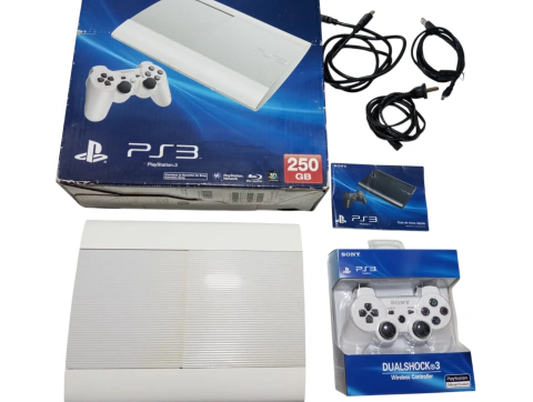 Consola Sony PlayStation 3 Super Slim en su caja original, edición limitada Classic White de color blanco, junto a un joystick inalámbrico nuevo en blíster cerrado azul, cable de corriente, cable de carga y cable HDMI sobre fondo blanco.