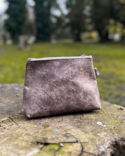 Neceser Rufina gris con textura mate, colocado sobre un tronco de árbol en un parque