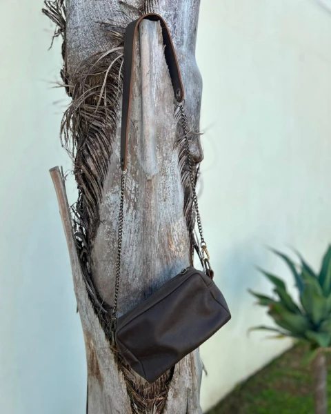 Cartera Bravía color chocolate colgada en un tronco de árbol, con correa de cadena y cuero marrón oscuro

