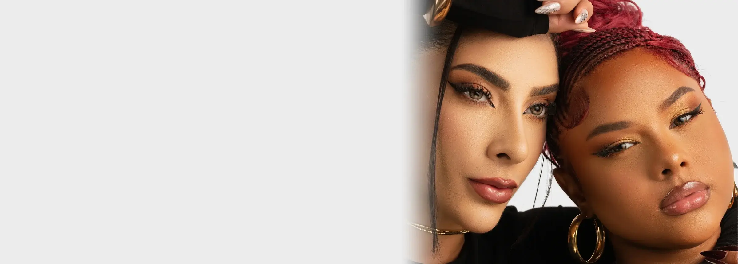 Duas modelos de rosto colado, uma de cabelo preto e outra de tranças vermelhas, com argolas douradas