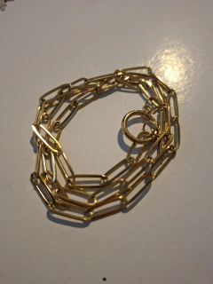Cadena dorada tipo paperclip enrollada sobre fondo blanco