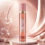 Frasco de Body Splash Vanilla Shimmer Isabelle La Belle 300ml com partículas de brilho em fundo rosado com flores e pérolas