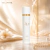 Frasco branco elegante do Body Splash Diore Fem Isabelle La Belle 300ml sobre superfície brilhante com pérolas e flor ao fundo