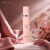 Frasco rosa claro do Body Splash La Vida Es Bella Isabelle La Belle de 300ml em fundo com tecido rosa acetinado e flores secas rosas