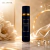 Frasco preto elegante do Body Splash Nice Girl Isabelle La Belle com detalhes dourados, em superfície refletiva ao lado de flor branca e tecido dourado