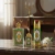 Kit Queen of Arabia da Lattafa Perfumes com frasco de perfume, frasco pequeno e spray perfumado com design verde e dourado, sobre mesa de mármore com flores brancas ao fundo