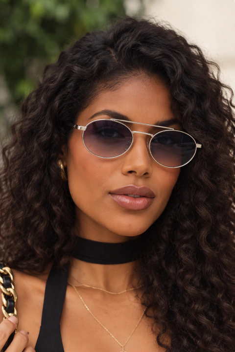 Mulher usando óculos de sol redondos Milano com armação metálica prateada e lentes escuras.