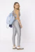 Modelo usando top fitness cinza com detalhes nas costas, combinando com leggings cinzas e mochila azul.
