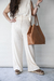 Una mujer sosteniendo un bolso de cuero marrón llamado Bolso Cookies, vistiendo un conjunto blanco de pantalones anchos y blusa sin mangas.