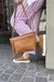 Zapatillas de cuero color marrón con suela blanca, combinadas con pantalones de rayas rosas y una cartera de cuero marrón.