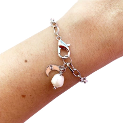 detalhe no pulso da pulseira semijoia energética banhada a ródio com pingente de Lua esmaltada em cor salmão e pérola para trabalhar a intuição feminina