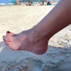 detalhe no tornozelo da tornozeleira semijoia com pingente moedas e ponto luz banhado a ouro 18k