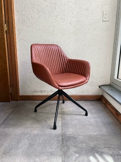 Sillón Rivel de ecocuero en color suela con diseño giratorio y respaldo reclinado, ubicado en un ambiente moderno.