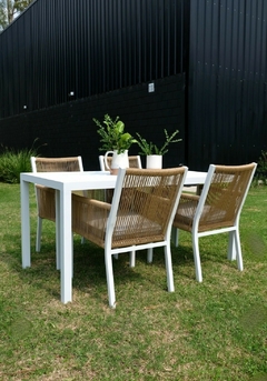 Mesa de comedor blanca con cuatro sillones de aluminio y cuerda, decorada con plantas.