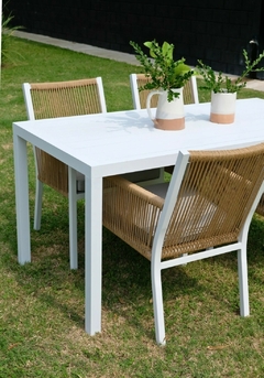 Mesa de comedor blanca con cuatro sillones de aluminio y cuerda, decorada con plantas.