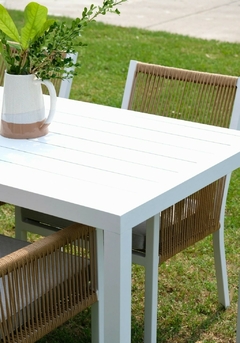 Mesa de comedor blanca con cuatro sillones de aluminio y cuerda, decorada con plantas.