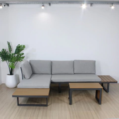 Set de sillón exterior en forma de L con estructura metálica negra, cojines grises y mesas laterales de madera