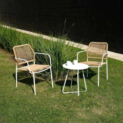 Dos sillas de exterior con diseño moderno y una mesa blanca de centro, ubicadas en un jardín con césped y plantas verdes.