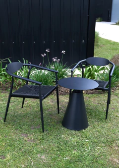 Silla Cipre de aluminio negro para exterior con asiento tejido, junto a mesa baja negra en jardín con césped y flores