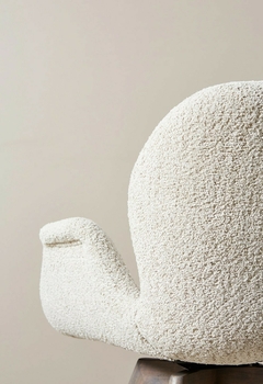 Silla tapizada en bouclé de color claro junto a una mesa de madera con un cuenco decorativo.