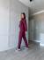 Mulher vestindo conjunto moletinho vinho com calça e blusa, em ambiente interno com parede cinza clara e piso de madeira