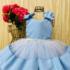 Vestido de festa infantil azul com detalhes em tule e pérolas, exposto em um suporte de vestido.