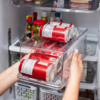 Organizador para latas em uma geladeira, com latas vermelhas sendo retiradas por mãos.