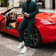 Hombre vestido con traje formal slim fit verde junto a un auto deportivo rojo.