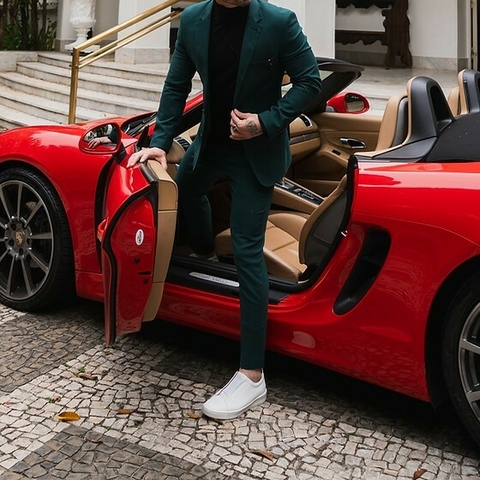 Hombre con traje formal slim fit verde saliendo de un auto deportivo rojo.