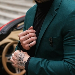 Hombre vistiendo un traje formal slim fit verde, con un fondo de un automóvil y detalles de tatuajes en las manos.