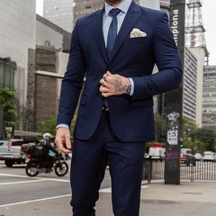 Hombre luciendo un traje formal slim fit azul turquí, con una camisa blanca y corbata de puntos, en un entorno urbano.
