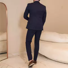 Hombre vestido con traje azul marino y zapatos marrones de cuero, visto de espaldas en una habitación con sofá blanco y espejo grande.
