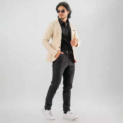 Hombre joven con blazer sport beige slim fit, camisa negra, pantalones oscuros y tenis blancos