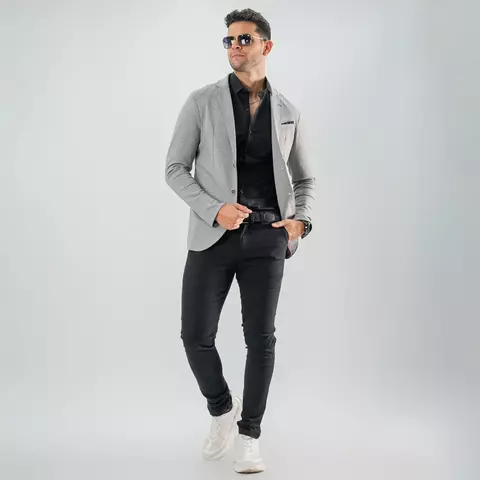 Hombre joven con gafas de sol usando blazer sport gris perla slim fit combinado con camisa negra, pantalones ajustados negros y zapatillas blancas