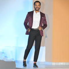 Hombre sonriendo con un blazer jacquard vino tinto, camisa blanca y pantalones negros, posando con confianza.