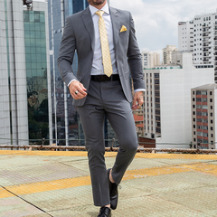 Hombre caminando con traje formal slim fit gris oscuro, camisa blanca y corbata amarilla con lunares, en un entorno urbano.