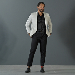 Hombre posando con un blazer premium slim fit color tiza, camisa negra y pantalones oscuros, en un fondo gris.