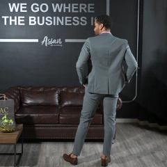 Hombre de pie vistiendo un traje gris, de espaldas, en un ambiente de oficina moderna con un sofá marrón y una pared con texto inspirador.