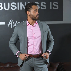 Hombre con traje gris y camisa rosa, posando con confianza en un entorno profesional.