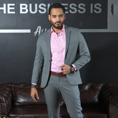 Hombre de pie en un traje gris con camisa rosa, mostrando un estilo elegante y moderno.