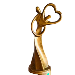 Estatueta dourada em gesso representando casal de almas gêmeas segurando um coração