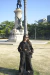 Mulher usando calça pantalona preta Sombra Boa com blusa preta e óculos escuros em praça com monumento ao fundo