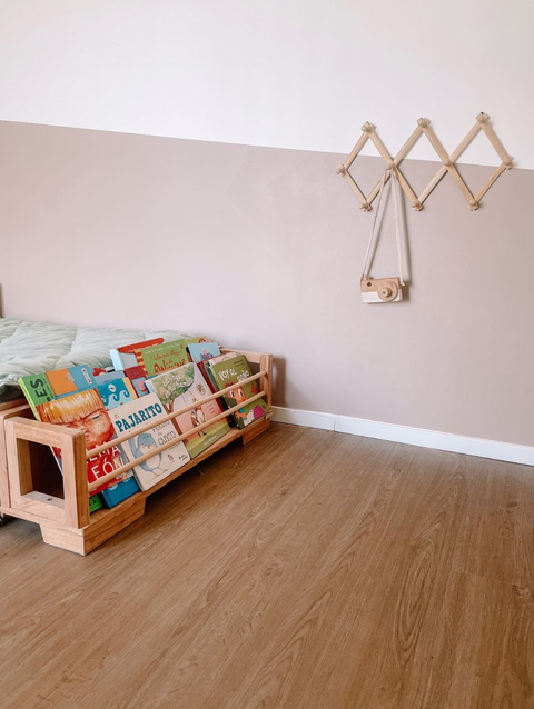 Vista de una biblioteca de madera con libros infantiles en un ambiente acogedor, junto a una cama.