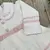 Vestido de saída maternidade para menina em tricô branco com detalhes em rosa, com gola bordada e laço decorativo