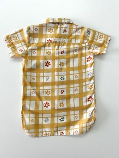 Camisa alongada com estampa floral em fundo amarelo e quadrados brancos.