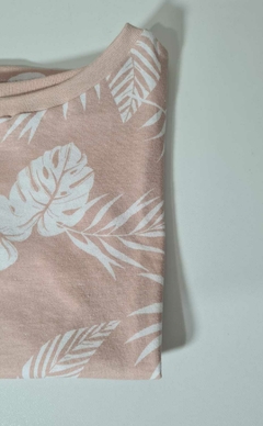 Camiseta floral dobrada em tom rosa claro com estampas de folhas brancas.