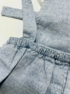 Detalhe da jardineira azul jeans com listras, mostrando alças e parte da cintura.