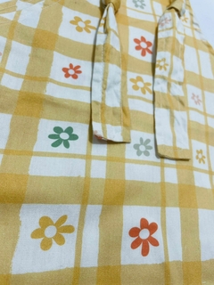 Jardineira floral em amarelo com estampas de flores coloridas e padrão quadriculado.