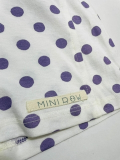 Jardineira branca com poá lilás da marca Mini Row, destacando o detalhe das bolinhas e a etiqueta da marca.